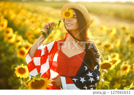 Beautiful girl in hat with the American flag in a sunflower field. 4th of July. Fourth of July. Freedom 127091631