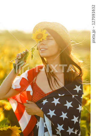 Beautiful girl in hat with the American flag in a sunflower field. 4th of July. Fourth of July. Freedom 127091632