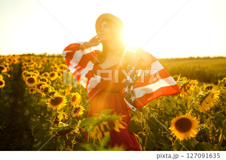 Beautiful girl in hat with the American flag in a sunflower field. 4th of July. Fourth of July. Independence Day. 127091635