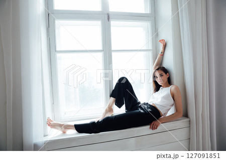 Slender fashion woman sitting at the window in a white room 127091851