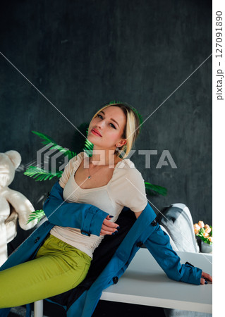 Beautiful blonde woman in green pants sitting on a white table Beautiful blonde woman in green pants sitting on a white table 127091890