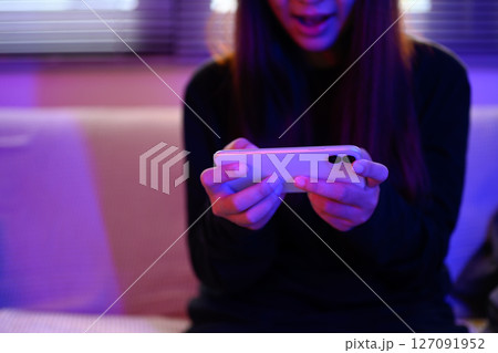 Young woman excited while playing mobile game with vibrant colored lighting Young woman excited while playing mobile game with vibrant colored lighting 127091952