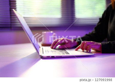 Close up of hands typing on a laptop under ambient purple lighting 127091998