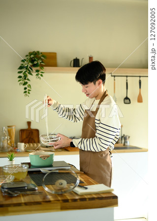 Smiling man in apron preparing noodles in a cozy home kitchen 127092005