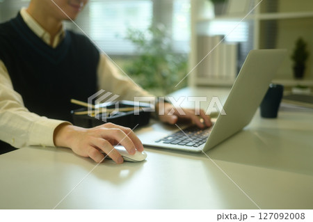 Close up of man using a laptop and mouse while having lunch at a desk 127092008