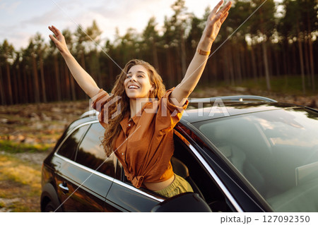 A young woman feels freedom leaning out of a car window in a sunny forest. Travel concept. 127092350