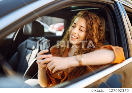 Happy woman in the car in the driver's seat looks at the smartphone. Business, technology concept. 127092370