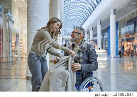 A woman is carefully placing a warm blanket over a man seated in a wheelchair A woman is carefully placing a warm blanket over a man seated in a wheelchair 127093637