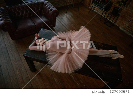 An elegant and graceful ballerina posed on a dark table surrounded by soft tutu fabric 127093671