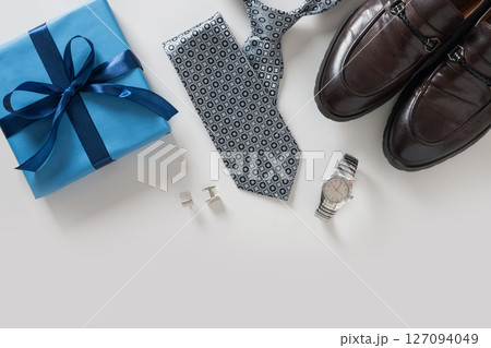 Happy Fathers Day greeting card with gift box. Set of classic mens clothes - brown shoes, wrist watch, necktie and blue gift on gray background. Men's accessories set. Top view. Copy space. Happy Fathers Day greeting card with gift box. Set of classic mens clothes - brown shoes, wrist watch, necktie and blue gift on gray background. Men's accessories set. Top view. Copy space. 127094049