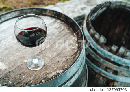 Glass of Red Wine on Old Oak Barrel in Rustic Cellar 127095708