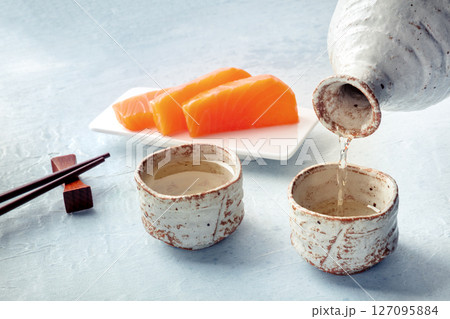 Sake poured into ochoko, traditional cup, with salmon sashimi 127095884