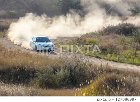Rally Car Completes a Sharp Turn on a Dusty Road 127096997