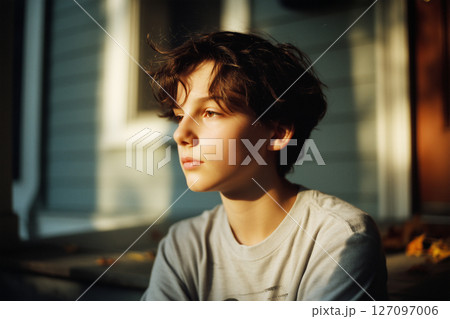 A young boy with brown hair and a white shirt is sitting in the sun 127097006