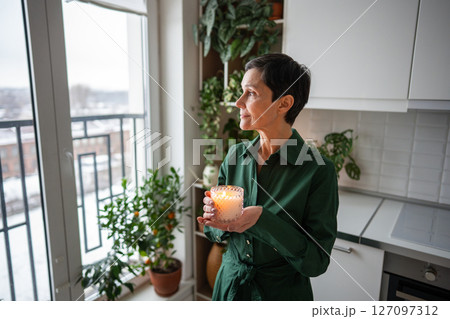 Aromatherapy rest. Content woman holding lit scented candle, relaxing alone at home after work Aromatherapy rest. Content woman holding lit scented candle, relaxing alone at home after work 127097312