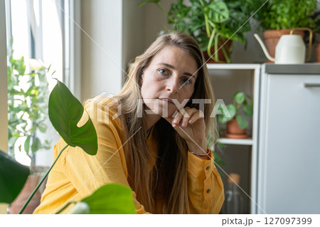 Portrait of thoughtful serious middle aged woman surrounded by indoor plants, looking at camera 127097399