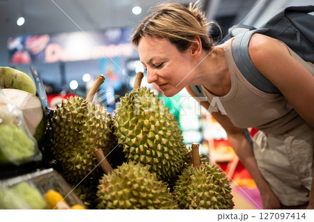 Unhappy woman wrinkles nose sniffing stinky durian on fruit counter, strong odor cause repulsion Unhappy woman wrinkles nose sniffing stinky durian on fruit counter, strong odor cause repulsion 127097414