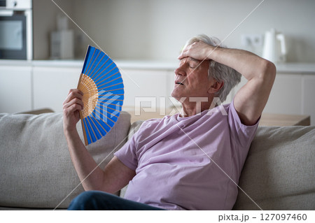 Older man struggling with fan heat exhaustion. Pensioner try to cope in sweltering home in summer 127097460