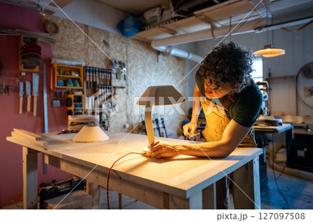 Skilled woodworker examining handmade lamp detail. Checking red wire connection, custom design diy Skilled woodworker examining handmade lamp detail. Checking red wire connection, custom design diy 127097508