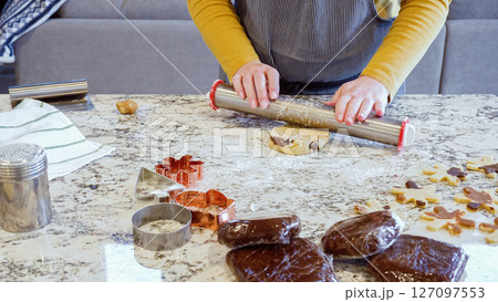 Using an adjustable rolling pin to roll out gingerbread cookie dough on the elegant marble counter in a modern kitchen, getting ready for festive holiday baking. 127097553