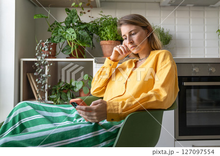 Restless woman browsing phone feed checking updates during downtime at home among house plants Restless woman browsing phone feed checking updates during downtime at home among house plants 127097554