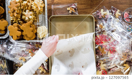 Flat lay. Carefully packaging Christmas cutout cookies, half-dipped in chocolate, sprinkled with crushed nuts, and presented in clear cellophane wrapping. Flat lay. Carefully packaging Christmas cutout cookies, half-dipped in chocolate, sprinkled with crushed nuts, and presented in clear cellophane wrapping. 127097565