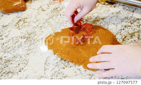 Using various festive cookie cutters, we're cutting out charming gingerbread cookies from the rolled dough on the sleek marble counter, bringing holiday cheer to the modern kitchen. Using various festive cookie cutters, we're cutting out charming gingerbread cookies from the rolled dough on the sleek marble counter, bringing holiday cheer to the modern kitchen. 127097577