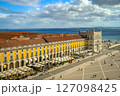 Wide shot of Commerce Square or Praca do Comercio in Lisbon, Portugal, iconic yellow Pombaline architecture, bustling outdoor cafes, Tagus River, city life, historic downtown, sunny day, sky with 127098425