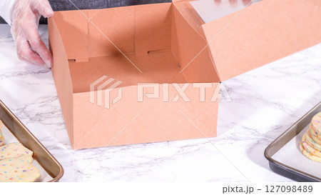 The sugar cookies, filled with sprinkles mixed into the dough, are carefully arranged with meticulous precision into a rustic brown paper box. 127098489