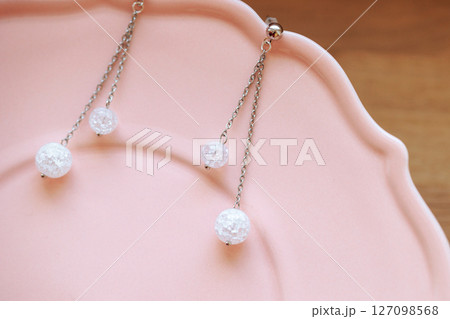 Silver chain earrings with clear crackle beads on pink plate over warm wooden background Silver chain earrings with clear crackle beads on pink plate over warm wooden background 127098568