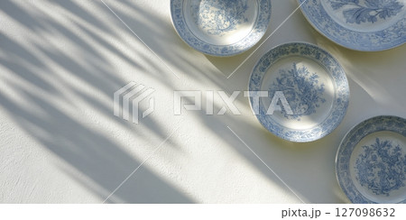 China plates cast shadows on a sunlit garden wall, displaying vibrant patterns and textures 127098632