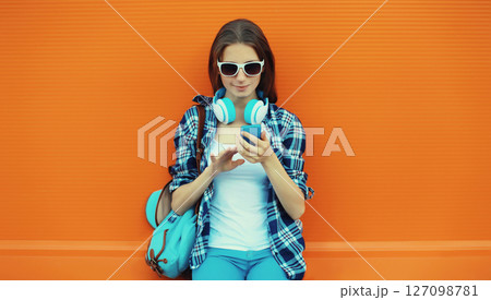 Modern young woman listening to music with smartphone, girl in headphones holding phone 127098781