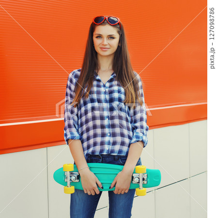Summer portrait of happy cheerful stylish young woman with skateboard posing on red background 127098786