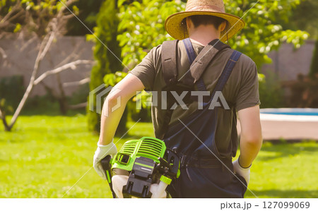A man with a lawnmower cares for the grass in the backyard. 127099069
