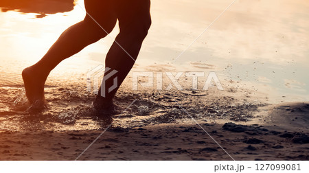 A man is running along the coast, training, legs and water closeup. A man is running along the coast, training, legs and water closeup. 127099081