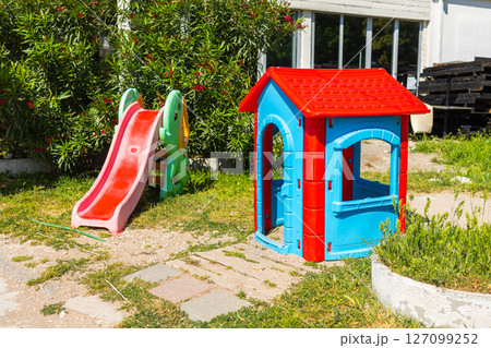Colorful plastic playhouse and slide on green grass. Outdoor recreation, children play area, and summer leisure environment. 127099252