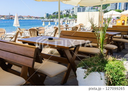 Wooden benches and tables at beach cafe under umbrella. Coastal hospitality, summer relaxation, and outdoor seating near sea. Wooden benches and tables at beach cafe under umbrella. Coastal hospitality, summer relaxation, and outdoor seating near sea. 127099265