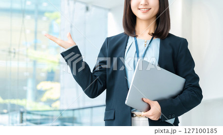 パソコンを持って案内をする笑顔の女性・ビジネスウーマン パソコンを持って案内をする笑顔の女性・ビジネスウーマン 127100185