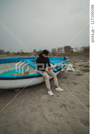 Man Reads A Book In Solitude By The Sea On A Gloomy Day 127100386