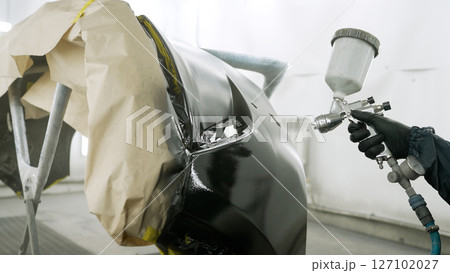 Mechanic painting car bumper in auto repair shop Mechanic painting car bumper in auto repair shop 127102027
