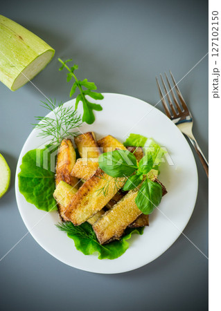 Homemade fried zucchini on a white plate on a gray background Homemade fried zucchini on a white plate on a gray background 127102150