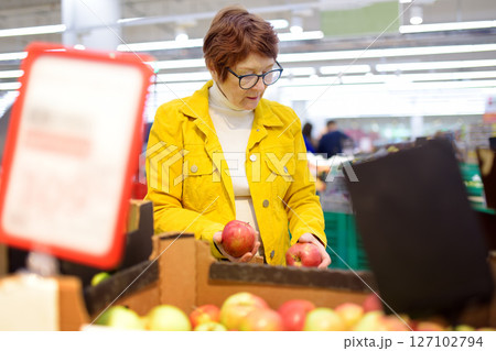 Beautiful red-haired senior lady is choosing fresh organic apples in a food store or a supermarket . Beautiful red-haired senior lady is choosing fresh organic apples in a food store or a supermarket . 127102794