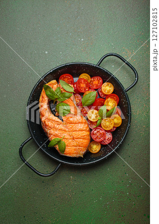 Grilled salmon steak with cherry tomatoes and basil leaves in black pan with cutlery top view on dark green background Grilled salmon steak with cherry tomatoes and basil leaves in black pan with cutlery top view on dark green background 127102815