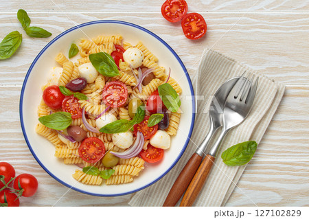 Italian pasta salad with fusilli, cherry tomatoes, mozzarella, olives, basil on white wooden background top view, Italian cuisine Italian pasta salad with fusilli, cherry tomatoes, mozzarella, olives, basil on white wooden background top view, Italian cuisine 127102829