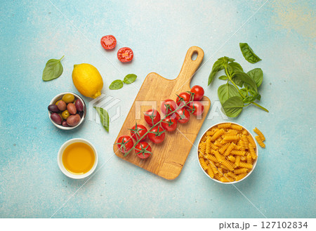 Fresh cherry tomatoes, fusilli pasta, basil, olives and olive oil creating Italian or Mediterranean cuisine and cooking scene on blue background top view 127102834