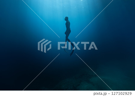 Freediver Swimming in Deep Sea With Sunrays. Young Man Diver Eploring Sea Life. Freediver Swimming in Deep Sea With Sunrays. Young Man Diver Eploring Sea Life. 127102929