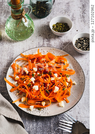 Homemade carrot slices in spices with ricotta and pumpkin seeds on a plate vertical view 127102962