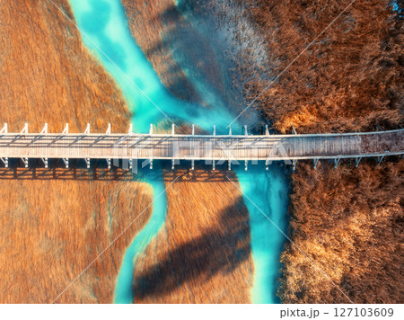 Aerial view of wooden bridge, azure river and orange grass 127103609