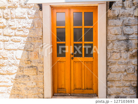Bright wooden door with frosted glass panels set in a stone wall. Mediterranean architecture, warm tones, and traditional exterior detail. Bright wooden door with frosted glass panels set in a stone wall. Mediterranean architecture, warm tones, and traditional exterior detail. 127103693