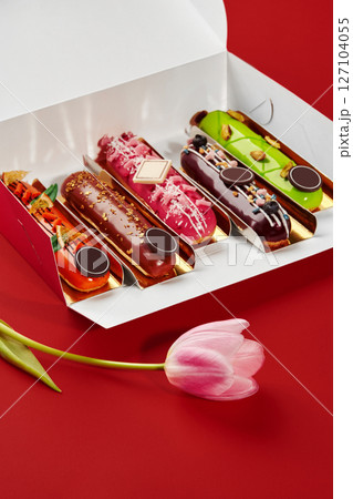 Box of colorful eclairs with tulip on red background Box of colorful eclairs with tulip on red background 127104055